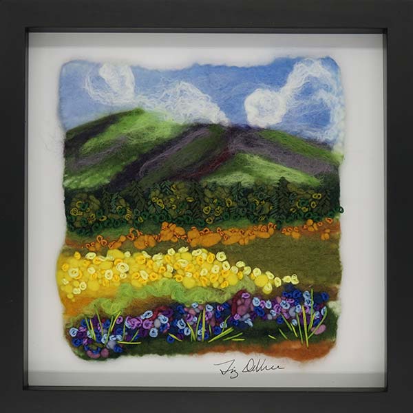 Felted textile landscape scene with mountain in background and bright flowers in front.
